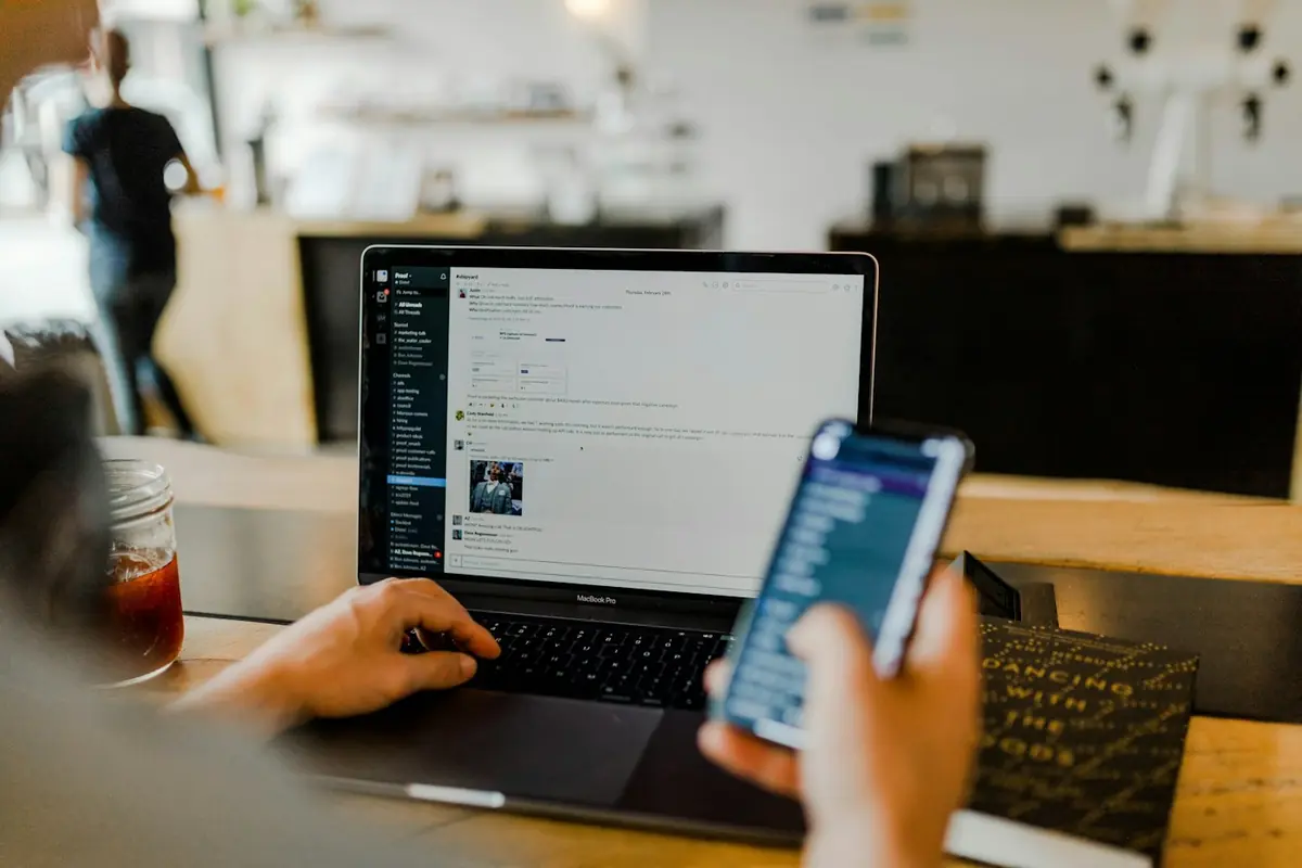 Empresária respondendo mensagens no celular ao lado do notebook